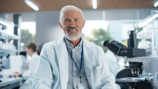 Middle Aged Genetic Research Scientist Using a Microscope in an Applied Science Laboratory. Portrait of a Handsome Senior Lab Engineer in White Coat Looking at Camera and Smiling