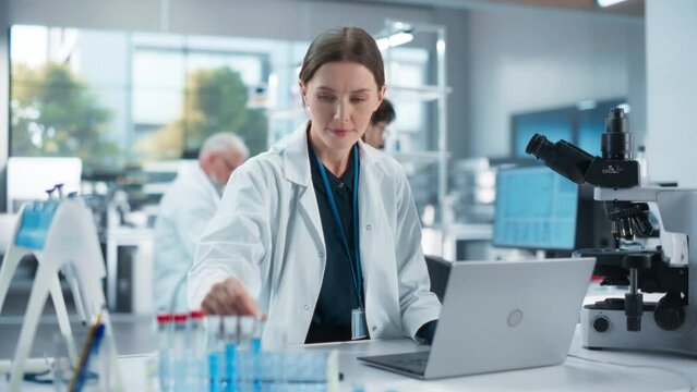 Caucasian Female Medical Research Scientist Work on a New Generation Medical Products in a Modern Laboratory. Young Woman Working on a Laptop Computer, Browsing Research Data Online