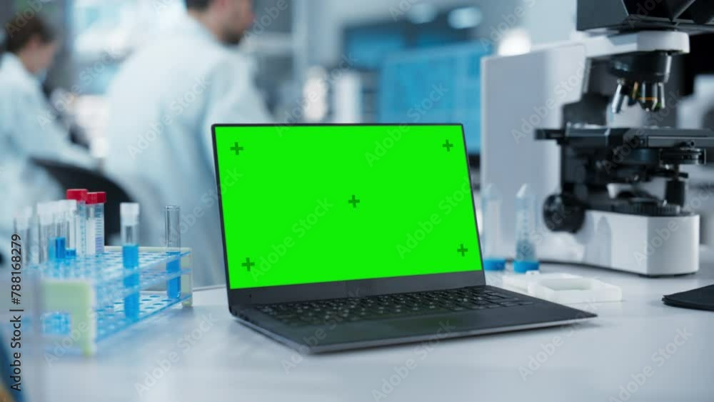 Leinwandbilder Laptop Computer with Green Screen Mock Up Display Standing on a Table in a Science Laboratory Next to a Microscope and Test Tubes with Biological Samples. Anonymous People Working in the Background