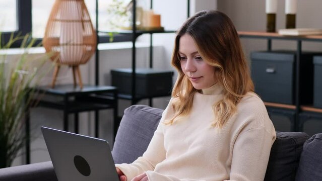 Cheerful Caucasian young Woman engaged in online entertainment, working, e-learning or chatting in social media with laptop at home living room. Spending leisure time.