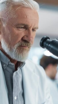 Vertical Screen: Senior Medical Research Scientist Looking at Biological Samples Under a Microscope in an Applied Science Laboratory. Portrait of a Middle Aged Doctor Working on a Research Project