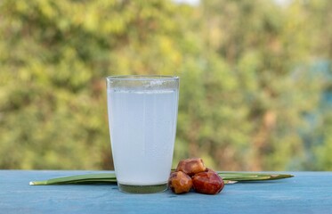 Khejur Ras or Date Palm Tree Juice in Glass with Phoenix Dactylifera Fruit with Leaves Isolated on Wooden Table Background with Copy Space, Also Known as Date Palm Sap or Khejur Rosh