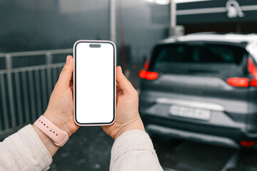 Hands with a blank phone screen on the background of a car wash