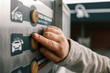 Close up of a hand pressing a button on a self-service coin machine at car wash - obrazy, fototapety, plakaty