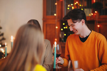Happy young friends clinking glasses of wine over table decorated for Christmas celebration