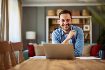 Portrait of a smiling adult man ready to work from home sitting in front of his laptop.