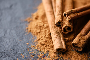 Cinnamon sticks and cinnamon powder on black slate plate close up. Studio macro shot. Food photography