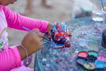 The background of a young child traveling with his family is painting a sculpture using a...