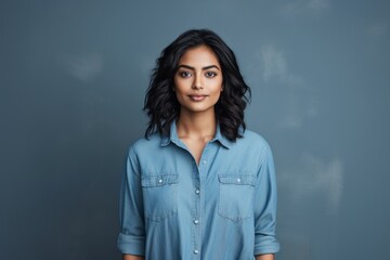 Obraz premium Portrait of a content indian woman in her 20s sporting a versatile denim shirt on minimalist or empty room background
