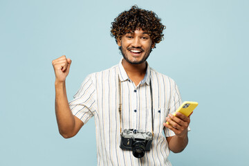 Traveler winner Indian man wears white casual clothes use mobile cell phone isolated on plain blue background. Tourist travel abroad in free spare time rest getaway. Air flight trip journey concept.