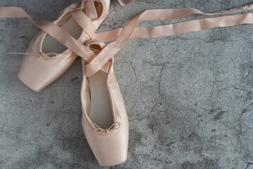 A pair of pink ballet slippers with a ribbon tied to the toe - obrazy, fototapety, plakaty