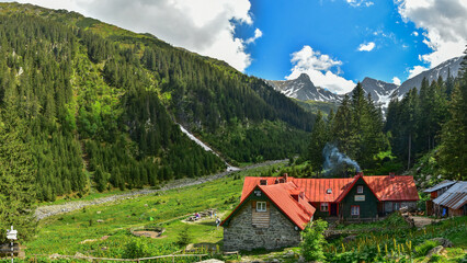 A mountain cabin located inside an alpine meadow, under massive, rocky mountain crests. Lots of...