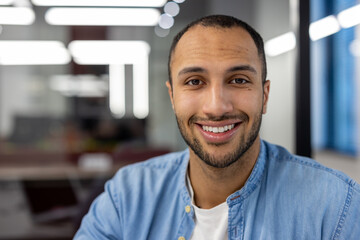 Close-up portrait of a Latin American man sitting in a modern office and smiling at the camera