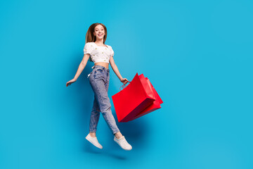 Full size photo of nice young girl shop bags jump empty space wear top isolated on blue color...