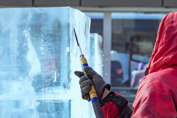 A sculptor processes a large ice cube with a sharp hand tool. Ice dust and ice fragments in the...