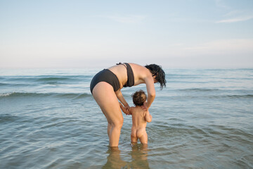 mother and baby daughter playing and having fun at the beach during the summer holiday in the mediterranean sea, wearing swimsuit. Bonding experience at sunset