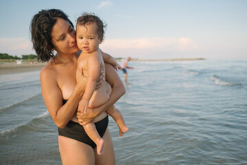 mother and baby daughter playing and having fun at the beach during the summer holiday in the mediterranean sea, wearing swimsuit. Bonding experience at sunset