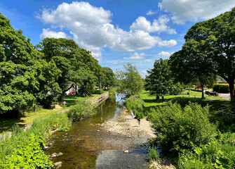 The River Aire meanders through a lush landscape, flanked by green trees and a bright blue sky in, Gargrave, Yorkshire, UK