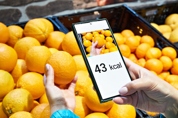 Checking calories on orange fruit in store with smartphone