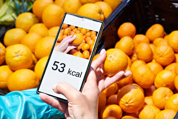 Checking calories on mandarin fruit in store with smartphone