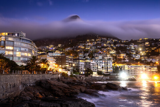 View of Bantry Bay city lights at night with low cloud over Lion&rsquo;s Head Mountain in background, Saunder's Rock beach, Cape Town, South Africa.