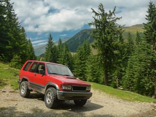 Driving an off road vehicle on high altitude mountainous roads. The jeep reached the alpine grasslands surrounded by coniferous forests. Carpathia, Romania.