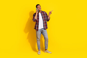 Fototapeta premium Full size photo of attractive man dressed plaid shirt talk on smartphone direting at offer empty space isolated on yellow color background