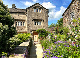 An English country garden, with a rustic stone house with a distinctive arched wooden door in the...