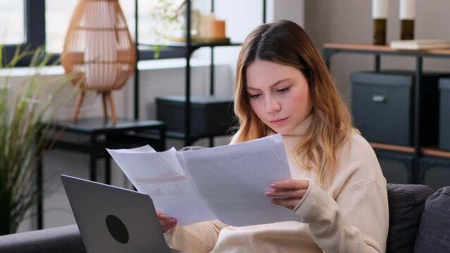 Focused Caucasian businesswoman working online with documents and laptop at home. Analyzing financial data and information. Student engaged in e-learning.