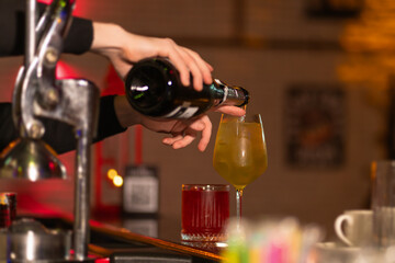 Close-up of the bartender carefully refills champagne into a glass of a ready-made cocktail with ice at the bar. Concept of making cocktails