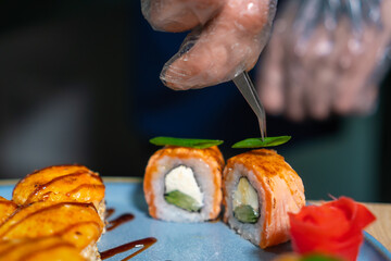 Close-up of the chef decorating baked sushi with small pieces of greens in the kitchen at the...