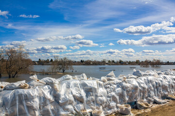 A wall of white sandbags has been erected as a barricade for flood protection, with a flooded embankment in the background.