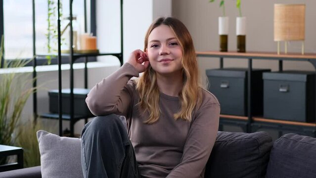Portrait of a Caucasian young content woman relaxing on sofa at home living room. Carefree lady spending weekend leisure time. Women individuality concept.