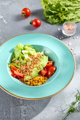 Fresh avocado salad bowl with corn, tomatoes, sweet pepper on a textured background with daylight
