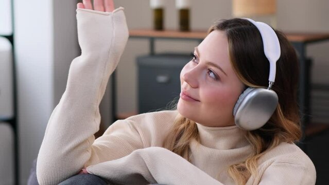 Joyful Caucasian young woman relaxing on sofa and enjoying leisure time with music in headphones. Retirement and recreation at home.