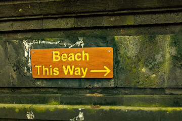 Beach this way arrow sign on the mossy stone wall in Bali, Indonesia