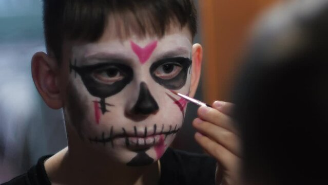 cute 10 year old boy draws makeup on his face to celebrate the Day of the Dead or Halloween. children's mystical image. Day of the Dead celebration