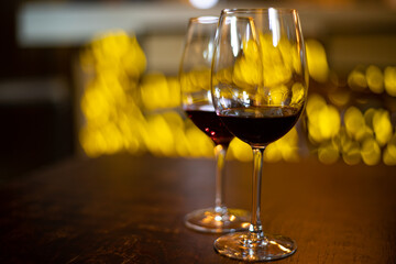 Two wine glasses on blurred light background, filled with red wine. Unevenly filled. Light creates reflections. Soft yellow bokeh background adds warmth. Focus on glasses, background blurred