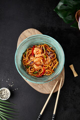 Chinese fried noodles with shrimps and vegetables in bowl on black concrete background. Modern composition with asian food - homemade noodles and shrimp in chinese style. Fried udon on wok with prawn - 788218465