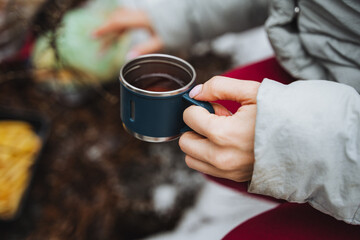 A small cup of tea in the hand of a woman on the background of the forest, a hiker on a hike holds...