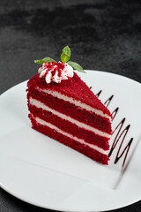 Red velvet cake on white plate on dark stone background. Popular red cake with layer biscuit and cream. Red velvet dessert in minimal style on black backdrop. Piece of cake with mint. - 788219261