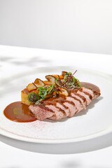Roasted duck breast with potato gratin and sauce on light background. Fried duck fillet on white plate with hard shadows Elegant summer menu. French cuisine - duck breast with gravy - 788219291