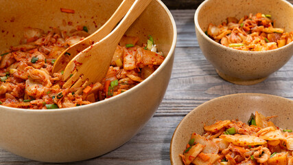 Serving kimchi, a traditional Korean side dish of salted and fermented vegetables with garlic, ginger, and gochugaru.  Wooden serving tongs in a big bowl.