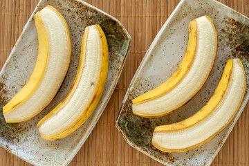 Top view of partially peeled bananas lying on two rectangular ceramic plates.
