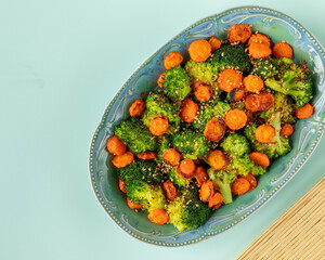 Top view of Asian-style stir-fried broccoli with carrot. Empty blue background, bamboo mat;