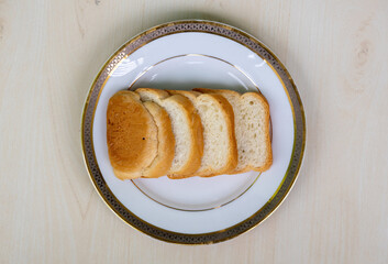 Bread slices on a white plate on wooden background. Top view