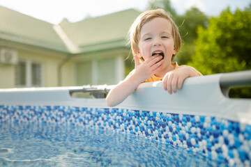 Cute funny toddler boy having fun by an outdoor pool. Kid playing with water. Family fun in a pool....