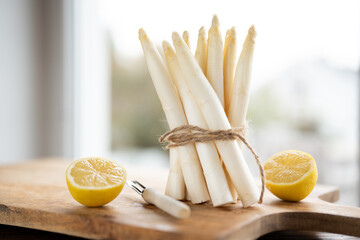 Bunch of fresh white asparagus. Seasonal spring vegetables with lemon on a wooden cutting board. Kitchen scene for the seasonal gastronomy.