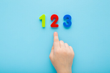 Baby boy hand finger pointing to colorful 123 numbers on light blue table background. Pastel color. Time to learning. Closeup. Top down view. - 788240810
