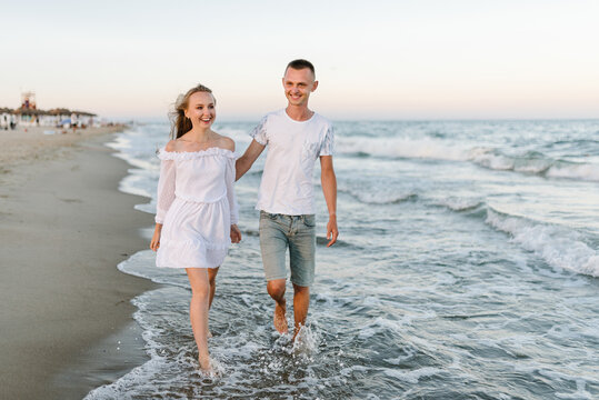 Barefoot on beach on water. Couple in love hugging on seashore. Female hugging male walking barefoot on water with big waves ocean and enjoying a summer day. Man embraces woman walks on sand sea.
